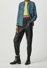 Modrá vzorovaná košile, žlutý crop top, černé kožené tepláky a černé kotníkové boty s texturovaným povrchem.