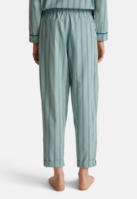 Gestreepte pyjamabroek in lichtblauw met verticale witte en donkerblauwe strepen. Zachte stof, elastische tailleband en omgeslagen broekspijpen.