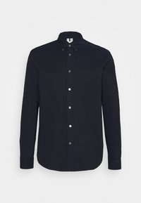 Chemise noire à manches longues avec boutons, col boutonné et poche poitrine, présentée sur un fond gris clair.