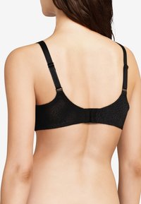 Reggiseno in pizzo nero con un design testurizzato, spalline regolabili e chiusura a gancio e occhiello sul retro. Presenta bordi scallopati.