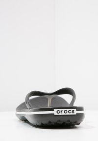 Svarta Crocs-sandaler med en texturerad yta, öppen bakdel och böjda remmar; har en vit accent och synlig varumärkeslogotyp på hälkappan.