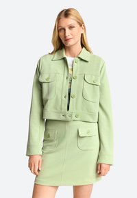 Cropped green jacket with two front pockets and a button closure. Soft material and structured collar. Paired with a matching skirt.