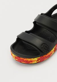 Černé sandály se dvěma nastavitelnémi pásky, vybavené texturovaným vnitřkem a podešví s plamenným vzorem v červené a žluté barvě.