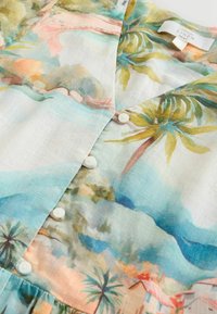 Blouse en lin à motif floral avec une palette de couleurs pastel claires, motifs de palmiers, col en V et boutons blancs sur le devant.