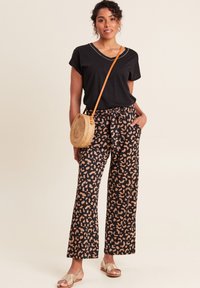 Zwarte top met korte mouwen en V-hals, gecombineerd met hooggerokte, wijde broek met een perzik- en zwarte panterprint. Geweven schoudertas.