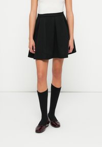 Fustă plisată neagră cu talie elastică, asortată cu șosete negre până la genunchi și balerini din piele patinată închisă. Design simplu, clasic.