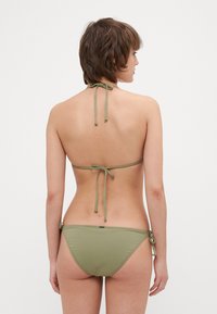 Olivgrön bikini, halterneck med knytband; baksidan har knutdetaljer. Slät tyg, minimalistisk design, lågmidja med sexiga bottnar.