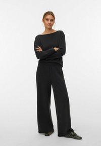 Ensemble de vêtements d'intérieur noir comprenant un haut ample à manches longues et encolure bateau, ainsi qu'un pantalon à jambes larges, tous deux confectionnés dans un tissu doux et lisse.