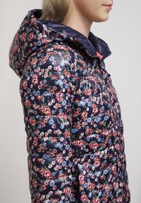 Giacca puffer floreale in navy con finitura lucida. Presenta sezioni trapuntate, un cappuccio e un motivo floreale in rosso, rosa e blu.