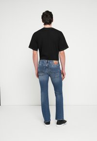 Must lühikeste varrukatega T-särk kontrastõmblustega, mida kannavad sinised teksapüksid. Teksadel on tagataskud ja vööjoonel silt.