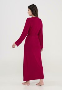 Bata larga ajustada en rojo vibrante, hecha de tela suave. Cuenta con mangas largas y un cinturón atado a la cintura, que llega hasta los tobillos.