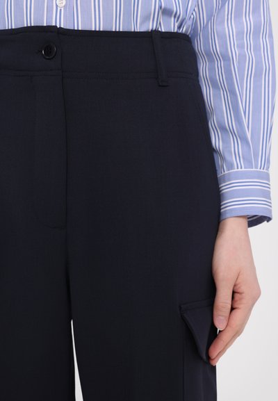 Pantalon bleu marine au design épuré, avec une fermeture à bouton, des poches latérales et une texture de tissu lisse. Assorti à une chemise rayée.