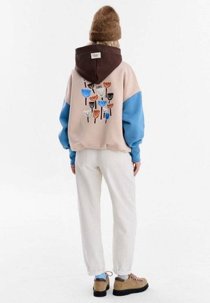 Bluza z kapturem w kolorze beżowym, niebieskim i brązowym z motywem kwiatowym na plecach. Połączona z kremowymi spodniami i beżowymi butami. Dzianinowa czapka z fakturą.