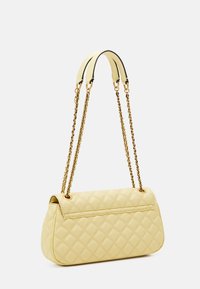 Żółta pikowana torebka na złotym łańcuszku, o zaokrąglonym kształcie i gładkiej skórzanej fakturze; minimalistyczny design bez dodatkowych ozdób.