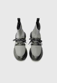 Gray knitted high-top sneakers with black rubber soles and laces featuring repeated branding. Smooth texture with a sock-like design.
