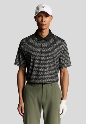 Sort-hvid mønstrede polo-shirt med sort krave, parret med olivengrønne bukser. En hvid kasket med et gult logo og en hvid handske bæres.