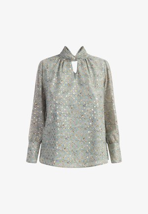 Valge rohelises kangas pika varrukaga pluus lillemustriga. Omab lõhikut kaeluses ja volangit õlgadel, et lisada tekstuuri.