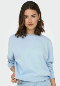 Lichtblauwe sweatshirt van zacht materiaal, met een relaxte pasvorm, ribbelmanchetten en een ronde halslijn. Gecombineerd met lichte denim.