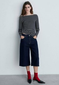 Un top cu mâneci lungi, cu dungi alb-negru, asociat cu culottes din denim închis și șosete roșii, completat cu tocuri negre ascuțite. Texturi lustruite.