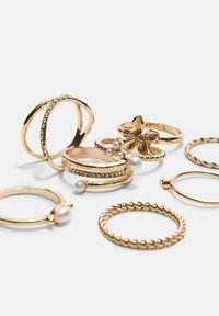 Set von goldenen Ringen mit verschiedenen Designs, darunter gedrehte Ringe, Perlenakzente, blumige Formen und Strassverzierungen.