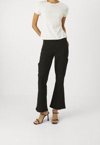 Jeans negros acampanados de denim, combinados con una camiseta blanca de algodón y sandalias de tacón de aguja negras, que muestran una silueta ajustada.