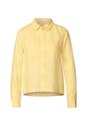 Camicia di lino gialla con colletto a bottoni, maniche lunghe e due tasche sul petto. Orlo leggermente arrotondato. Tessuto textured.