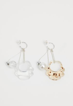 Jasne in bež smolnate uhane s krožnimi in zaobljenimi oblikami, opremljeni s srebrnimi dodatki in bisernimi detajli na verigah.