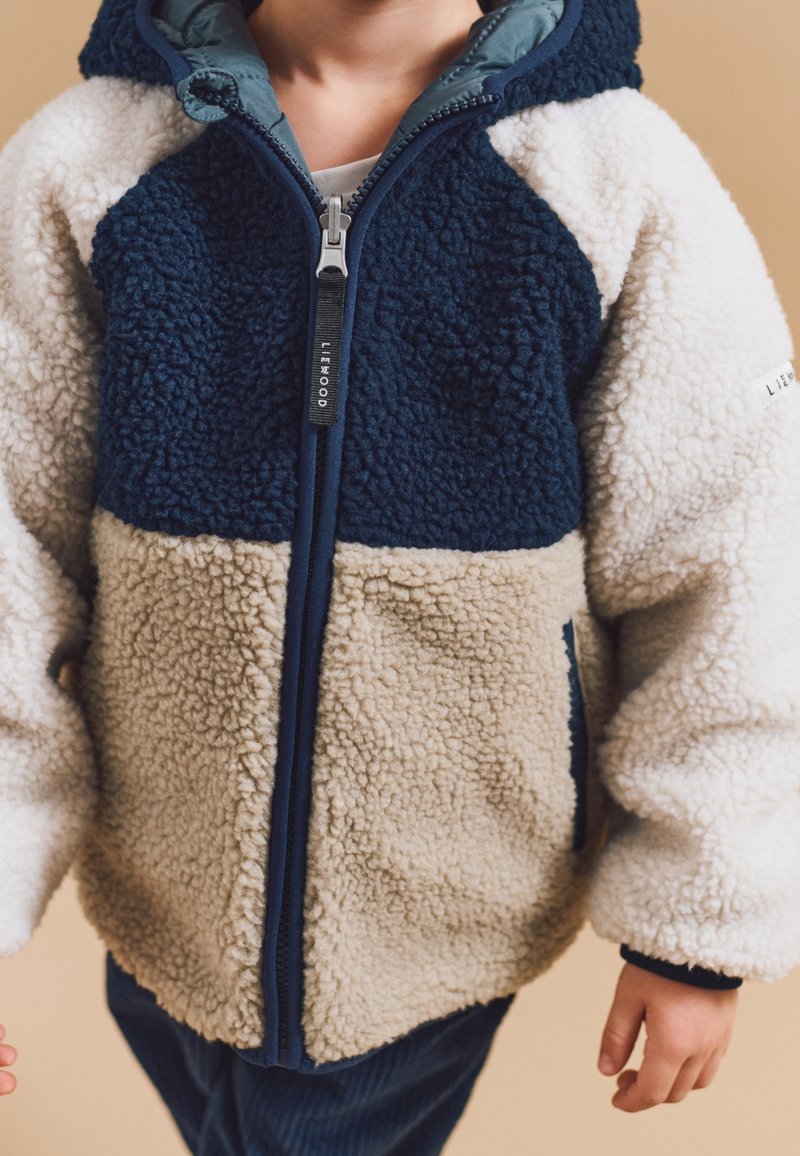 Fleece-Box-Jacke mit navyblauen, cremefarbenen und beigen Einsätzen. Strukturierter Stoff mit Kapuze und durchgehendem Reißverschluss. Beschichtete Details am Reißverschluss.