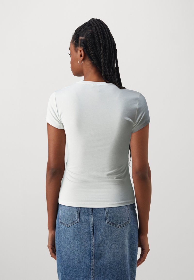 Jasnoniebieska dopasowana koszulka z krótkimi rękawami i okrągłym dekoltem, zestawiona ze spódnicą dżinsową. Gładka faktura z minimalną liczbą szwów.