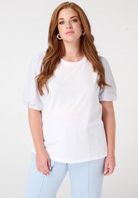 Haut blanc avec des manches courtes bouffantes rayées bleu clair et blanc. Tissu lisse, col rond, associé à un pantalon bleu clair.