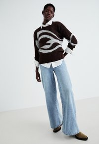 Brun og grå mønstrete genser laget av mykt materiale, kombinert med lyseblå vide jeans og brune ankelstøvler.