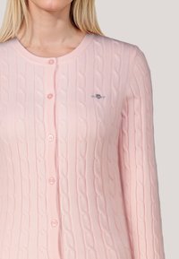 Rosa Strickcardigan mit Rundhalsausschnitt, langen Ärmeln und Knopfleiste, versehen mit einem kleinen, auf der Brust gestickten Logo.