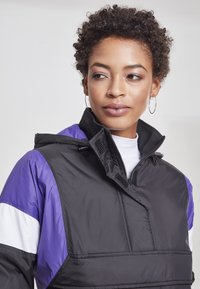 Jacheta anorak neagră și purpurie, cu guler înalt, design cu fermoar pe jumătate și panouri de accent albe. Material texturat cu finisaj mat.