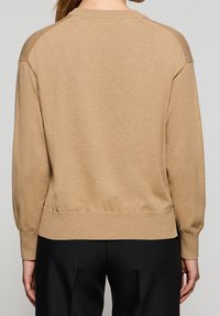 Pull-over en maille beige, doté d'un col arrondi, de poignets et d'un ourlet côtelés, avec une coupe légèrement ample et un tissu texturé sur les épaules.