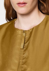 Golden brown zip-up top with a round neckline, featuring a smooth, shiny texture and a concealed zipper detail at the front.