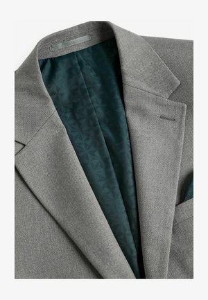 Hall hallitussärk, millel on tekstureeritud kangas. Sees on mustriline tumeroheline vooder. Märkimisväärsed detailid hõlmavad lapi kaelust ja taskut.