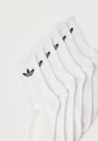 Λευκές βαμβακερές κάλτσες τοποθετημένες σε σειρά, με ριμπ υφή και μαύρο λογότυπο στο μανσέτο.