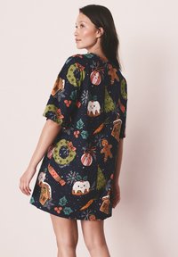 Tengerészkék ruha rövid ujjakkal, ünnepi mintákkal, például karácsonyfákkal, mézeskalács figurákkal, díszekkel és magyallevelekkel sötét alapon.