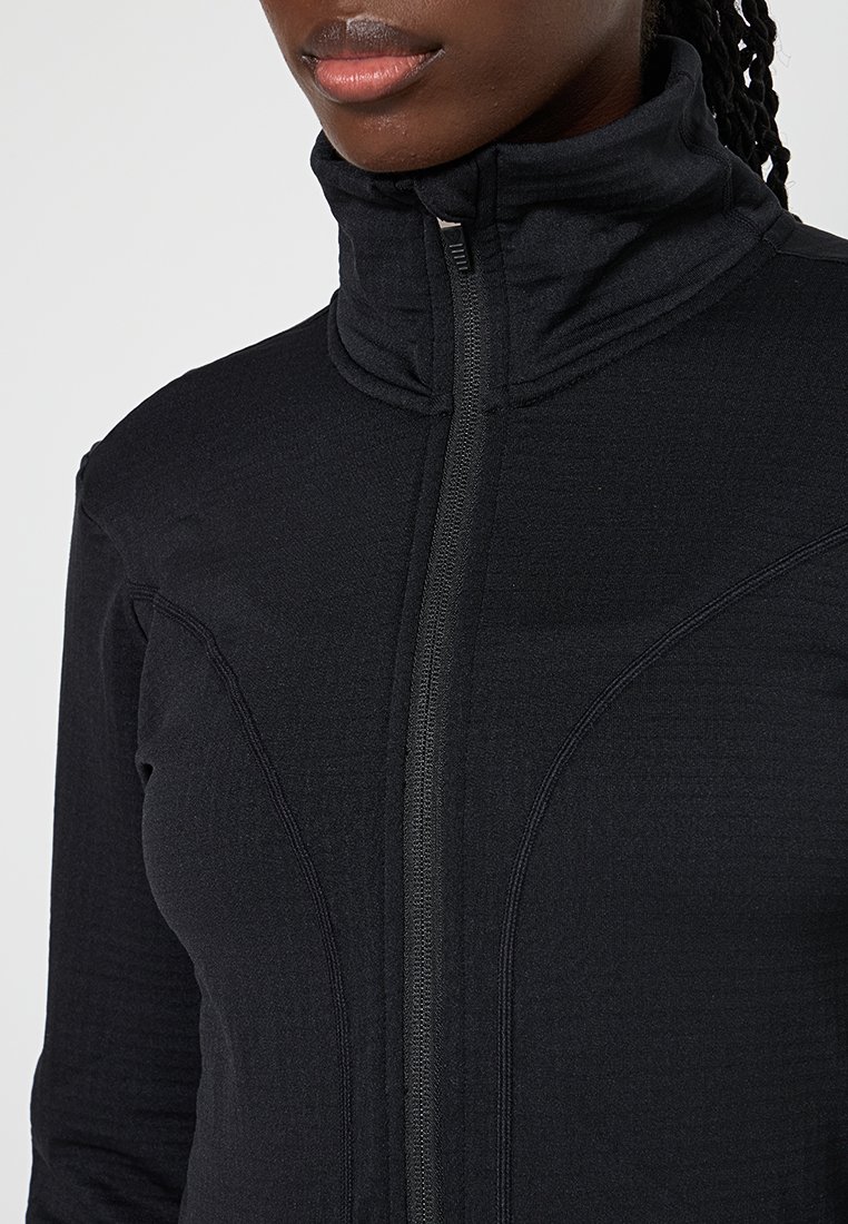 Schwarze Zip-Jacke mit hohem Kragen, gefertigt aus strukturiertem Stoff und mit geschwungenen Nähten. Der vollständige Reißverschluss ist vorne sichtbar.