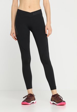 Leggings noirs avec taille haute, dotés de panneaux diagonaux et de trois bandes verticales contrastantes. Le matériau est extensible et lisse.