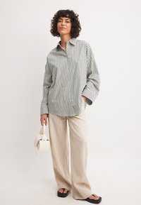 Striped button-up shirt in green and white, paired with light beige wide-leg trousers and black sandals. Holding a small white handbag.