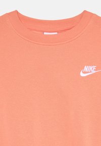 Pink cotton sweatshirt with a ribbed crew neck and a small white Nike logo embroidered on the chest. Soft texture and smooth finish.