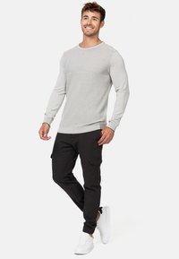 Suéter de manga larga color gris claro con textura de canalé y un patrón de rayas horizontales en la parte superior del pecho, combinado con pantalones cargo negros y zapatillas blancas.