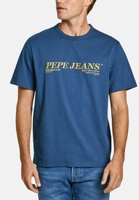 Mėlynas medvilninis marškinėliai su tekstu "PEPE JEANS" auksinės spalvos, apvaliu iškirpimu, trumpomis rankovėmis ir laisvu siluetu.
