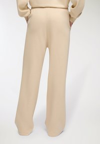 Beżowe spodnie typu wide-leg z miękkiego materiału o luźnym kroju. Posiadają ściągacz w pasie oraz boczne kieszenie dla większej funkcjonalności.