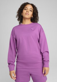 Felpa viola realizzata in morbido tessuto, con scollo a girocollo, spalle scese e una piccola patch con logo sul petto.