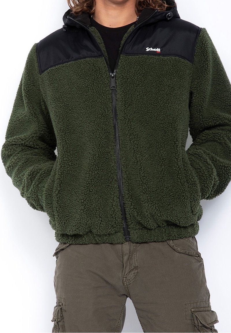 Giacca in pile verde con yoke in nylon nero, chiusura con zip sul davanti, cappuccio, orlo elasticizzato e tasche laterali. Tessuto testurizzato per il calore.