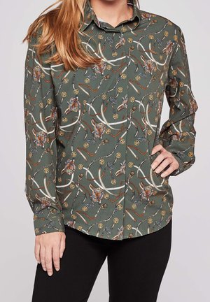 Camisa verde oliva con botones y mangas largas, con un estampado detallado de cuerdas, cadenas y amuletos en forma de estrella.