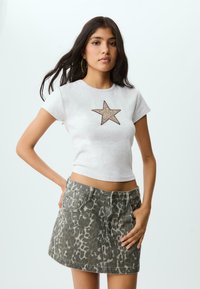 Grå kortærmet t-shirt med et glitrende stjernegrafik. Sammen med en tætsiddende denim mini-nederdel i et grønt leopardmønster.