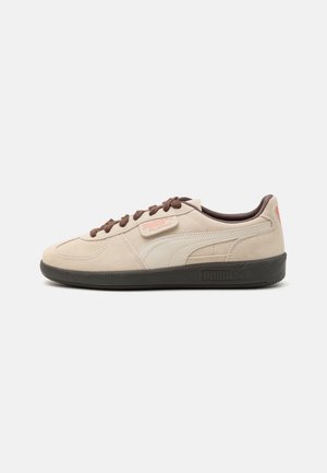 Beige suède Puma Palermo sneaker met bruine veters, zwarte zool en beige Puma logo streep aan de zijkant.